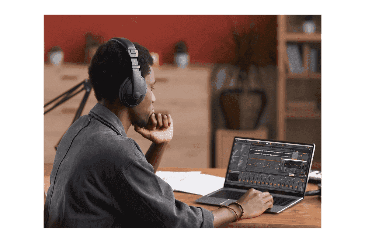 Produttore musicale con cuffie al lavoro su un laptop con software di produzione audio in uno home studio.